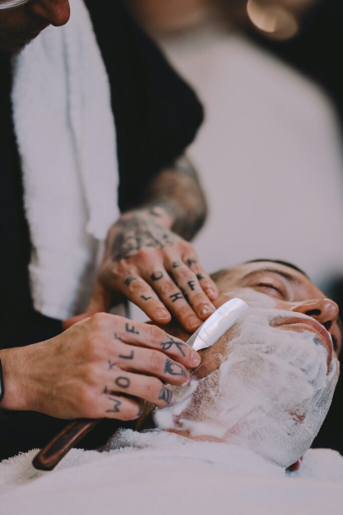 barber with tattoos shaving with a straight razor